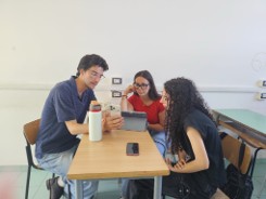 Nico sitting at a table with two students discussing information on a tablet
