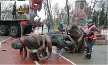 Workers remove a statue from its pedestal